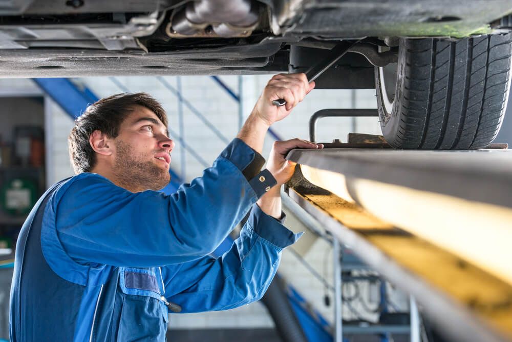 Technician in blue overalls looking under a car