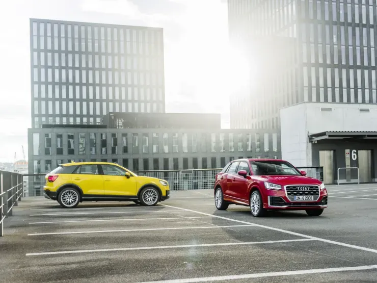 a yellow audi q2 shown from the side and a red audi q2 shown from the front side parked up in a city car park