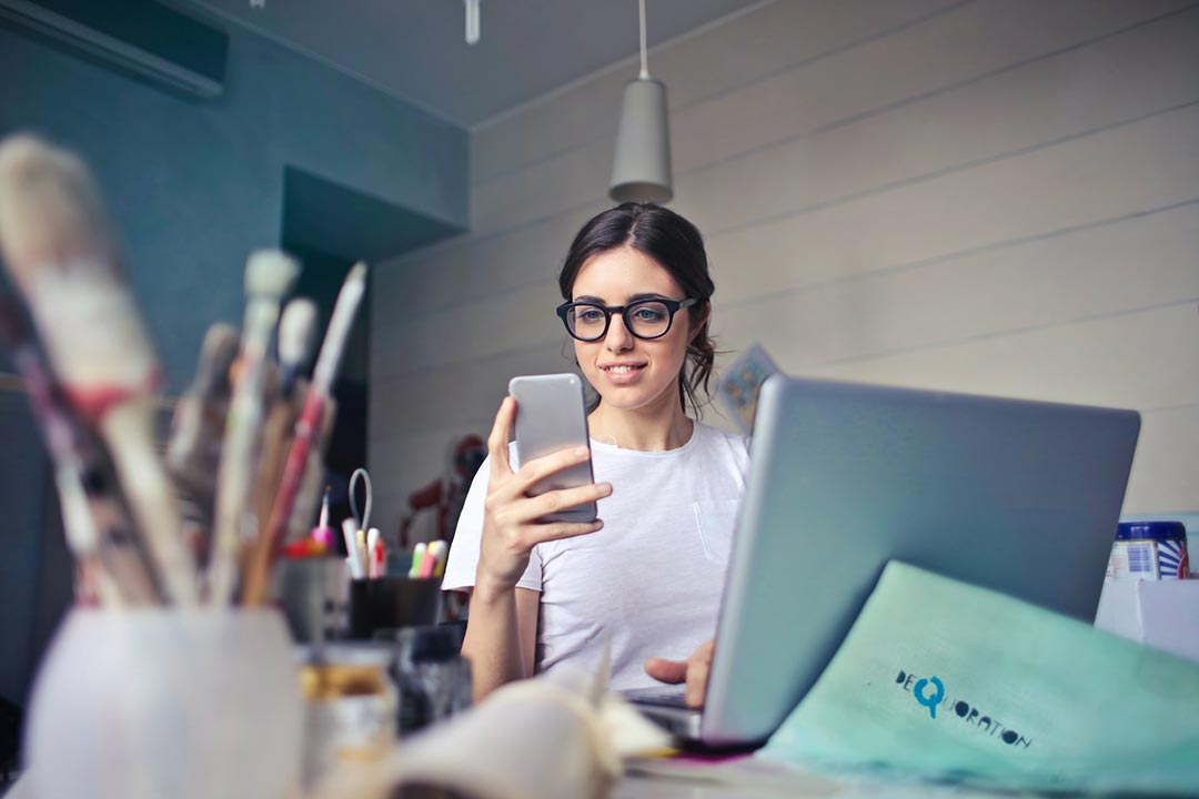 Women looking at phone in front of a laptop and paperwork